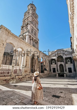 Rear view of young woman wearing stylish long dress standing in amazing square inside ancient  Diocletian palace in Split in Croatia  Royalty-Free Stock Photo #1992959429