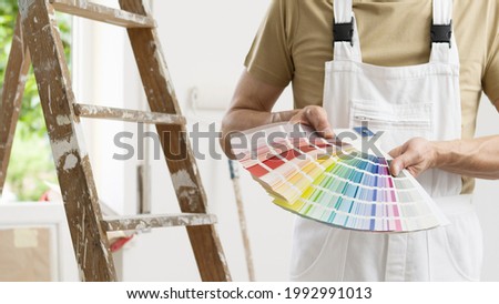hands of house painter man decorator choose the color using the sample swatch, work of the house to renovate, a wooden ladder and a green window as a background, close up