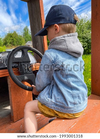 little caucasian boy wearing a baseball cap and hoody denim jacket sitting in wooden car pretend driving. Playground in countryside