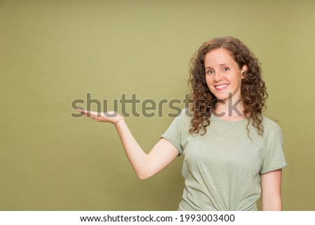 Portrait young redhead girl with curly hair smiling looking at camera with horizontal hand wearing green t-shirt on green background