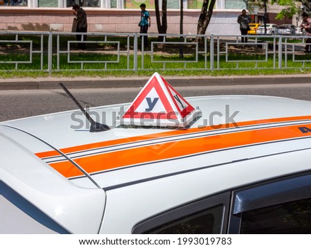 Triangular three-dimensional educational sign on the roof of a white car. The letter "У"of the Cyrillic alphabet means -"educational".