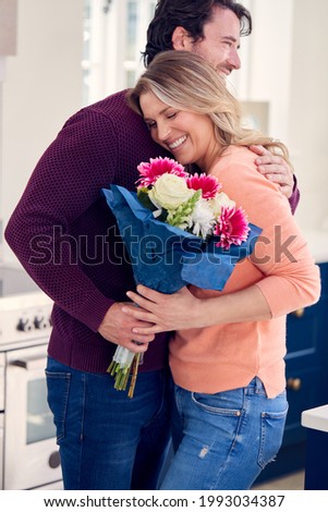 Man Giving Woman Bunch Of Flowers To Celebrate On Anniversary Or Birthday In Kitchen At Home