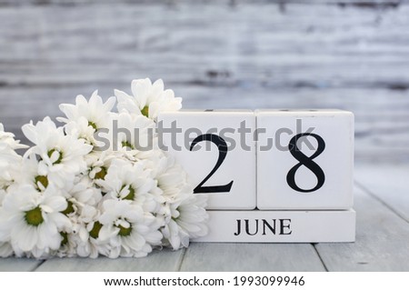 White wood calendar blocks with the date June 28th and white daisies. Selective focus with blurred background. 