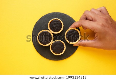 A picture of hand taking chocolate tart on slate plate and yellow background