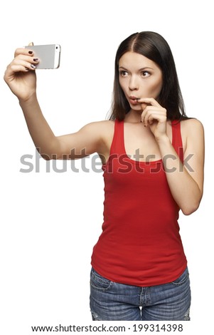 Happy surprised young girl taking pictures of herself through cellphone, over white background