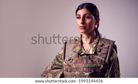 Studio Portrait Of Serious Young Female Soldier In Military Uniform Against Plain Background