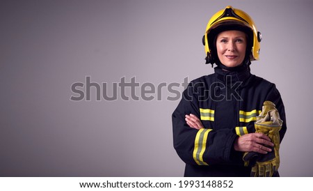 Studio Portrait Of Smiling Mature Female Firefighter Against Plain Background