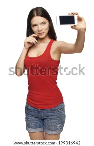 Happy young girl taking pictures of herself through cell phone, over white background