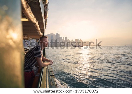 Pensive man looking from ferry boat against urban skyline st beautiful sunset. Tourist in Hong Kong.