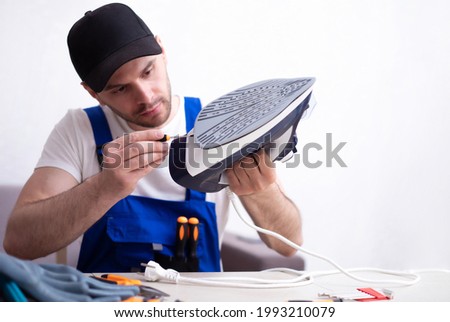 Close up photo of concentrated young man while he is fixing damaged iron on his workplace with tools