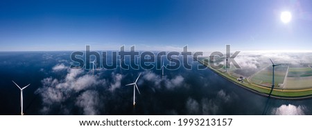 offshore windmill park with clouds and a blue sky, windmill park in the ocean aerial view with wind turbine Flevoland Netherlands Ijsselmeer. Green energy  Royalty-Free Stock Photo #1993213157