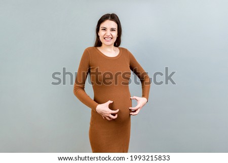 Pregnant woman scratching her belly on colored background. Royalty-Free Stock Photo #1993215833