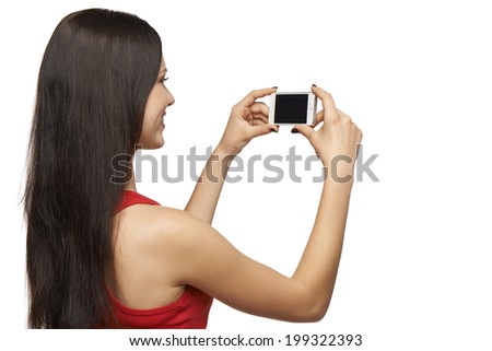 Happy young girl taking pictures of herself through cell phone, over white background