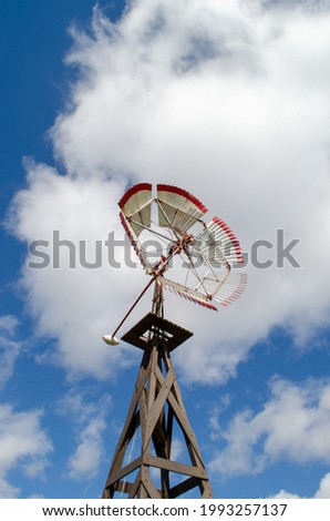 On this beautiful, cloudy day, a colorful windmill spins. It sits on top of a triangle patterned wooden stand.