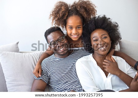 Portrait of happy young african American family with little kid sit relax on couch, smiling black parents rest on sofa hug preschooler children posing for picture at home together