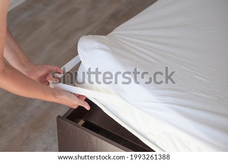 Bed with a high mattress. The woman puts on a protective water-repellent mattress cover. Royalty-Free Stock Photo #1993261388