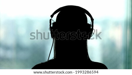 Back of woman wearing headphones on, silhouette of person listening to music, song, podcast, or audiobook
