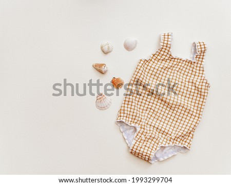 Summer background. Baby swimsuit with seashells on beige background, Holiday Flat lay, top view
