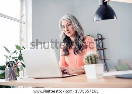 Photo of happy charming old businesswoman sit table look use laptop job office indoors inside house home