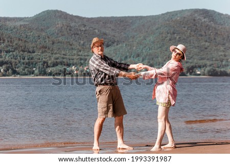 beautiful mature sportive couple walks along the sandy river bank on a summer sunny day with mountains in the background