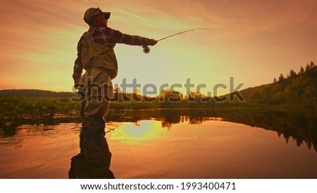 Fly fisherman stands in the water and fishing on the river at sunset