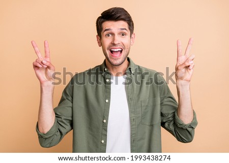 Photo of attractive happy amazed young man make v-signs good mood cool isolated on beige color background
