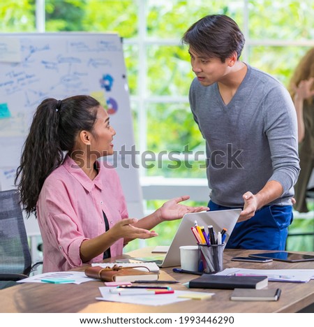 Closeup Two trendy casual Asian businesspeople explaining creative ideas and discussing marketing projects together, using laptop for searching information while sitting in comfortable modern office