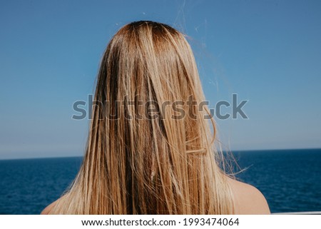 Back of blonde long-haired young woman watching blue sea horizont.