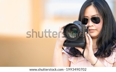 Amateur sunglasses Asian Woman take a photo with professional mirrorless camera at outdoor blue rooftop building in twilight time.