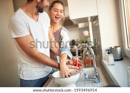 lovely young caucasian couple washing cherry tomato together, having fun in the kitchen