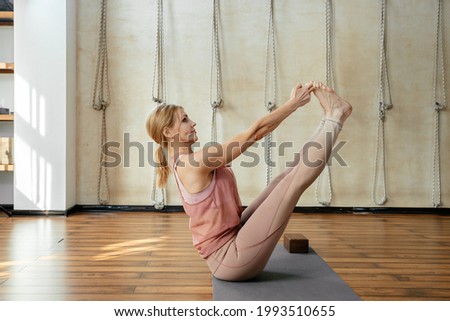 Mature strong woman doing yoga or pilates stretching relaxation exercise in white loft studio interior. Breathing, concentrating, healthy lifestyle concept