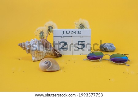 Calendar for June 25: cubes with the number 25, the name of the month of June in English, shells, sea stones, sunglasses, faded dandelions on a yellow background