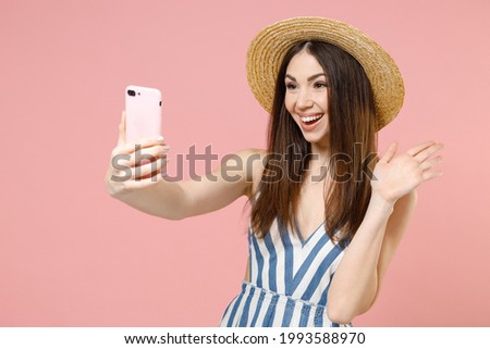 Young overjoyed happy woman in summer clothes striped dress straw hat doing selfie shot on mobile cell phone do winner gesture celebrating clench fist isolated on pastel pink color background studio.