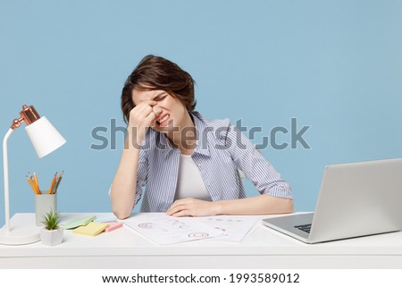 Young tired employee business director woman in casual shirt sit work at white office desk with pc computer laptop keep eyes closed rub put hand on nose isolated on pastel blue color background studio Royalty-Free Stock Photo #1993589012