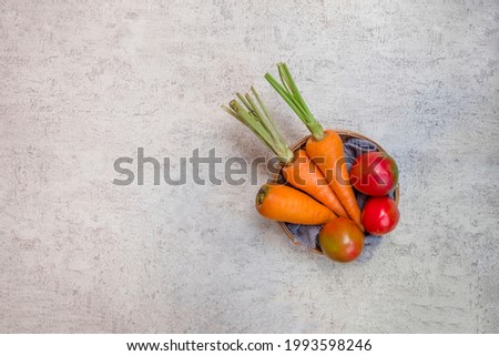 Group of raw carrots and tomatoes in a bamboo basket bowl isolated on grey abstract background