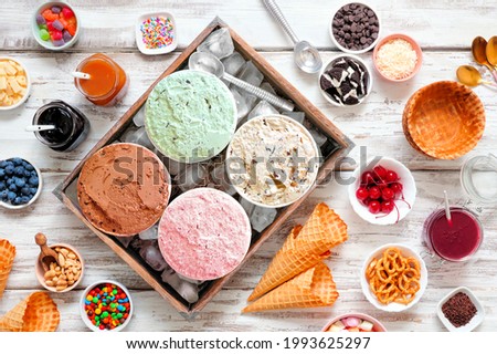 Summer ice cream buffet with a variety of ice cream flavors and sweet toppings. Overhead view table scene on a rustic white wood background.