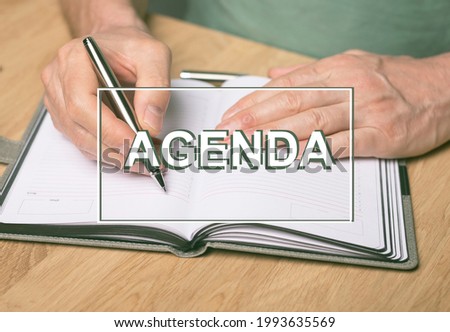 Agenda word. Inscription on photo of hands writing in planner or organizer.