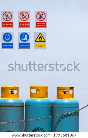 Gas cylinder tanks with various warning sign on white cement wall in safety zone area