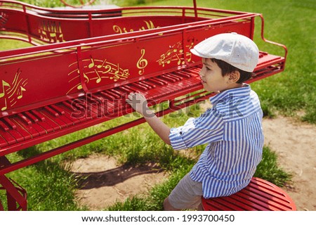 A school-age boy performs a song on a stationary red piano in the garden