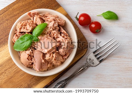 Top view of canned tuna in a bowl, fork and red cherry tomatoes on a white wooden table. Healthy eating snack of preserved tuna meat and fresh vegetables. Low calories tasty seafood. Close-up. Royalty-Free Stock Photo #1993709750