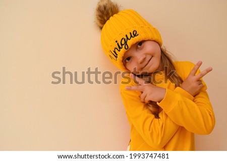 A cute little girl pulls on an orange cap with the words "unique" over her eyes and grimaces against. Copy space. A unique child. Children of the new generation. Fashionably dressed child