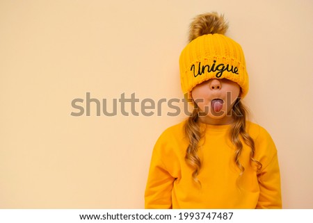 A cute little girl pulls on an orange cap with the words "unique" over her eyes and grimaces against. Copy space. A unique child. Children of the new generation. Fashionably dressed child Royalty-Free Stock Photo #1993747487