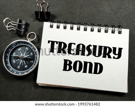 Finance concept.Text TREASURY BOND on notebook with paper clips and compass on black background.