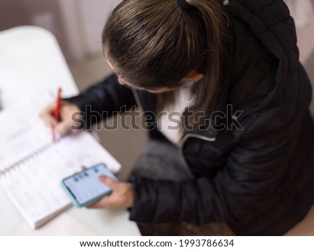 
Woman working from home, using pencil, notebook and cell phone. Taking notes communicating with customers via your smartphone. Blurred background.