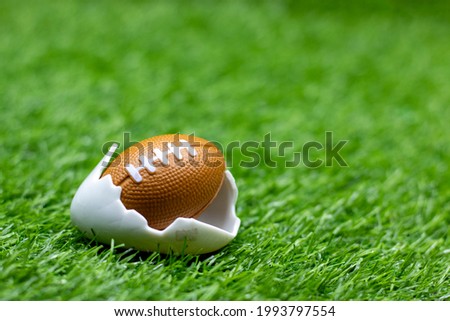 American football in egg shell on green grass background for Easter Holiday