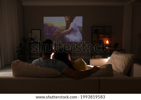 Couple watching movie on sofa at night, back view. Space for text