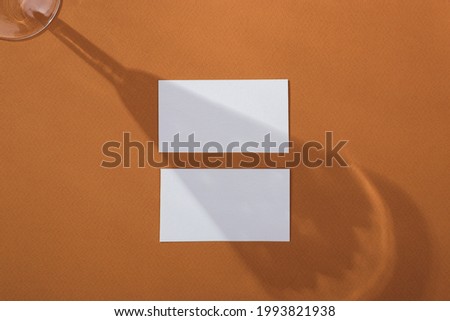 White empty paper card mockup for business card design design and artwork on brown background with abstract light and shadows from the wineglass
