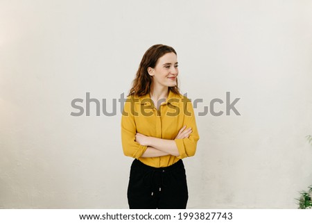 Interested intrigued young woman standing with folded arms against a white wall looking aside with a smile with copyspace Royalty-Free Stock Photo #1993827743
