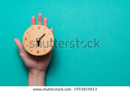 Hand of woman holding retro alarm clock on green table background, vintage style