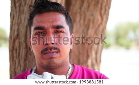 Portrait of Asian man in pink shirt with mask. After lockdown man sitting against a tree bark in a garden.